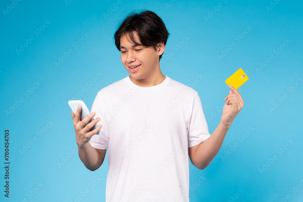Teen holding phone and credit card, blue background Teen holding phone and credit card, blue background