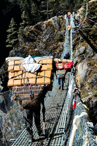 Vertical shot of a group of trekkers passing on the suspension bridge to the mountains photo