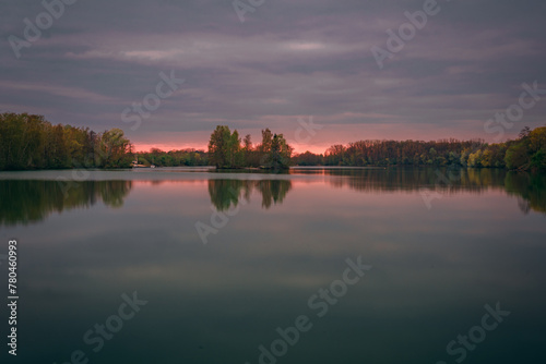 Beautiful sunset over the lake surrounded by trees which reflect in the water in Bavaria, Germany