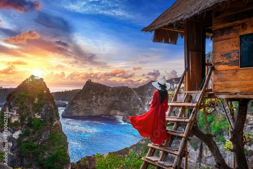 Female with a red the steps of a tree house at sunrise in Nusa Penida island, Bali, Indonesia photo