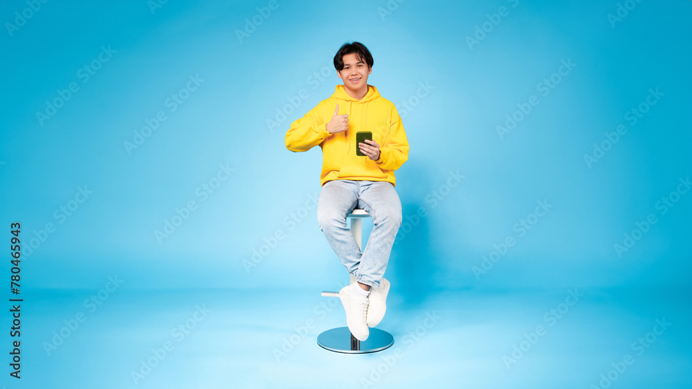 Obraz premium Cheerful young guy with phone gives thumbs up