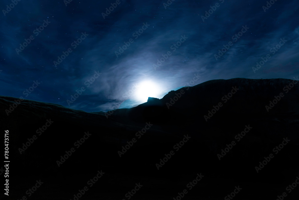 A mountain range is silhouetted against a dark sky with a bright moon