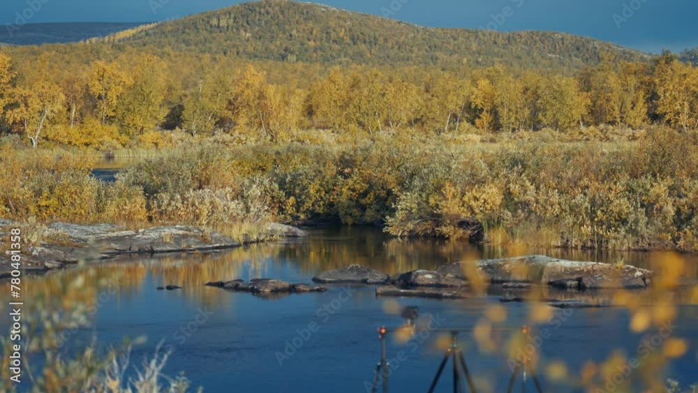 A professional camera mounted on a slider rig is positioned on the riverbank filming the autumn tundra landscape. A professional camera mounted on a slider rig is positioned on the riverbank filming the autumn tundra landscape.