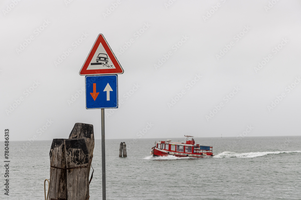 Traffic sign priority in oncoming traffic and attention roadside on the coast of the Venice Lagoon. Passenger ferry in the background