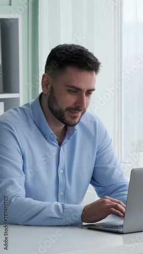 Concentrated Caucasian businessman, sitting at table and working online with laptop in office. Boss analyzing financial information. Vertical video.