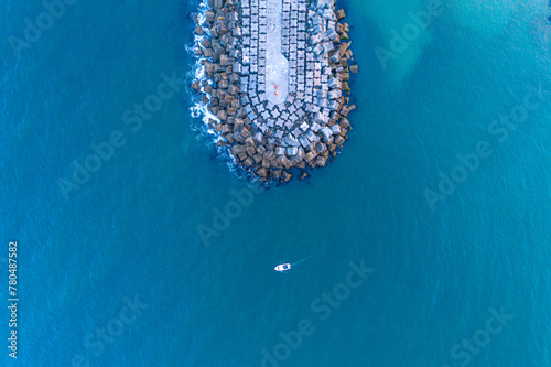a small fishing boat sailing near the breakwater of a harbor, aerial top view with a drone