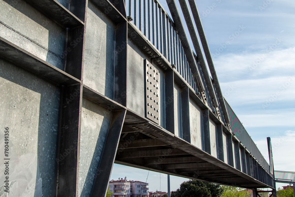 Close-up view of the steel structure of a modern bridge. Close-up of metal fence on the street. Detail of a steel bridge with blue sky in the background.