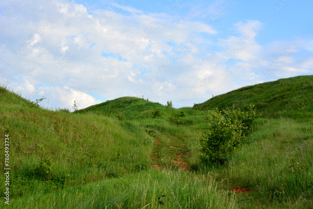 a green hill with a trail leading to the top and blue sky with clouds a green hill with a trail leading to the top and blue sky with clouds