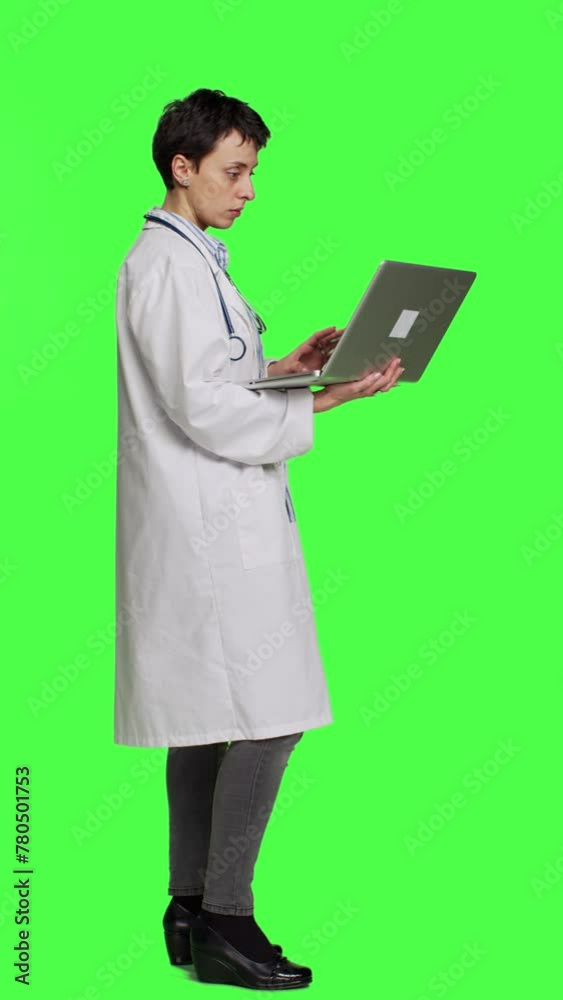 Profile Confident physician searching for new medicaments to treat disease, using laptop to browse on online web pages against greenscreen backdrop. Medic in white coat checks internet sites. Camera A Profile Confident physician searching for new medicaments to treat disease, using laptop to browse on online web pages against greenscreen backdrop. Medic in white coat checks internet sites. Camera A