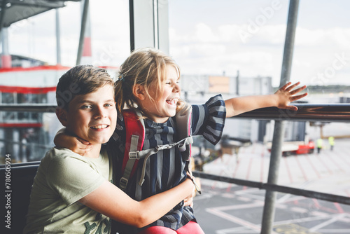 Little girl and school boy at the airport waiting for boarding at big window. Two kids stands at window against the backdrop of airplanes. Happy children, siblings leaving for family summer vacation photo
