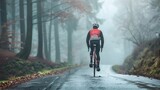 A cyclist in a red and black jacket with a white helmet riding a red and white bicycle on a wet foggy road lined with trees and fallen leaves.