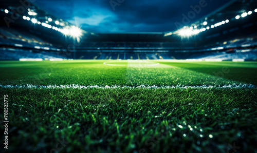 Illuminated sports stadium field at night, lush green grass glowing under bright floodlights, atmospheric evening scene