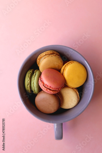 Purple cup filled with pastel macarons on pink background. Top view.