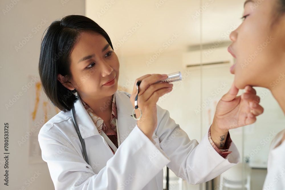 Smiling doctor examining mouth of patient with small flashlight Smiling doctor examining mouth of patient with small flashlight