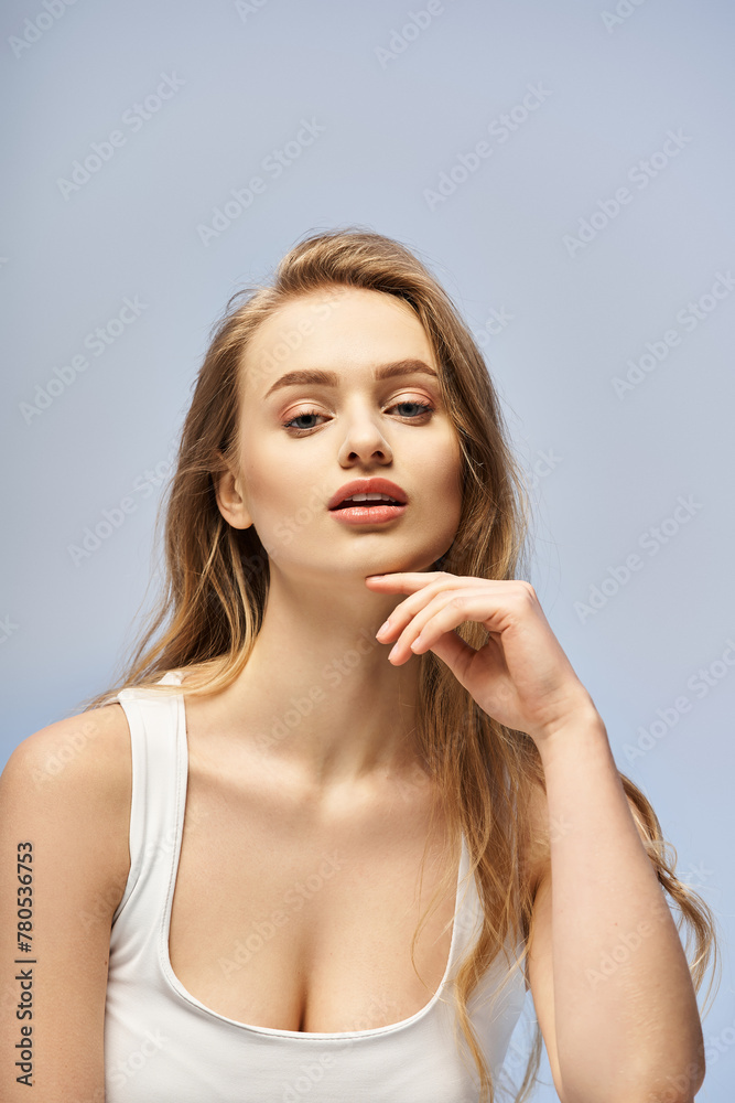 A blonde, young woman exudes elegance in a white top as she poses gracefully for the camera in a studio setting. A blonde, young woman exudes elegance in a white top as she poses gracefully for the camera in a studio setting.