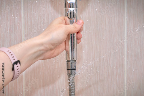 Laaking water hose close to shower head, water flow from the hole of the hose closeup. Broken shower hose, bathroom leaks, common water issues in home. Hand holding leaky hose.