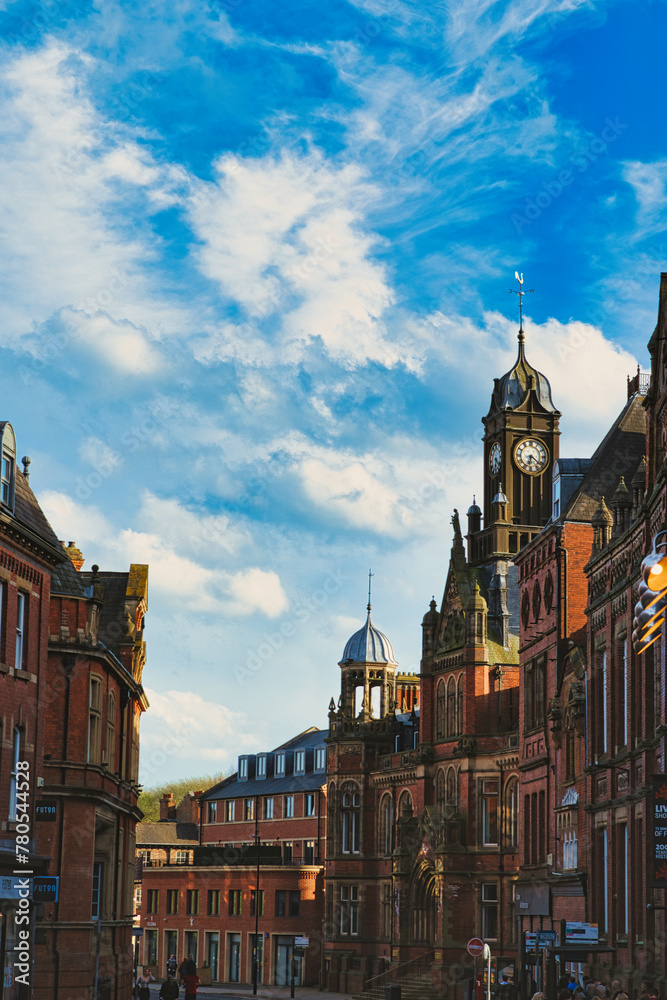 Vintage European architecture with a prominent clock tower under a vibrant blue sky with wispy clouds, capturing the essence of historic urban charm in York, North Yorkshire, England.