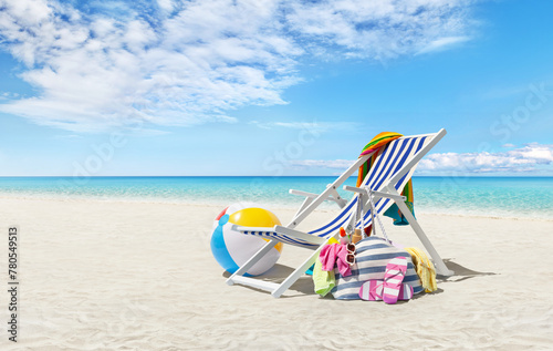 Beach deck chair for sunbathing on a sunny day by the seaside, beach ball and a bag full of accessories, concept of a summer beach holiday, online shopping, travel bookings, and resort accommodations