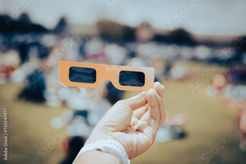 Asian hand wear smart watch holding paper solar eclipse with blurry crowd people watching totality show in Dallas, Texas, April 8, scratch resistant polymer lenses filter out harmful ultraviolet