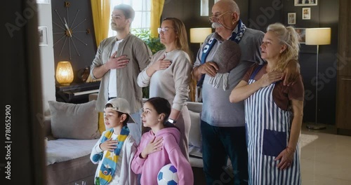 A multi-generational family of football fans stand in front of the TV and sing the national anthem before the start of the match photo