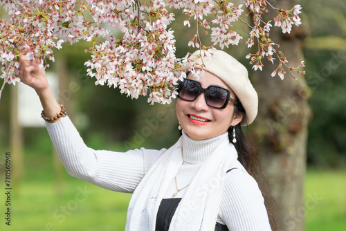 Portrait of a beautiful young Vietnamese woman against the background of cherry blossoms, sakura in pastel colors, who holds a sakura branch with her hand. Spring concept. photo