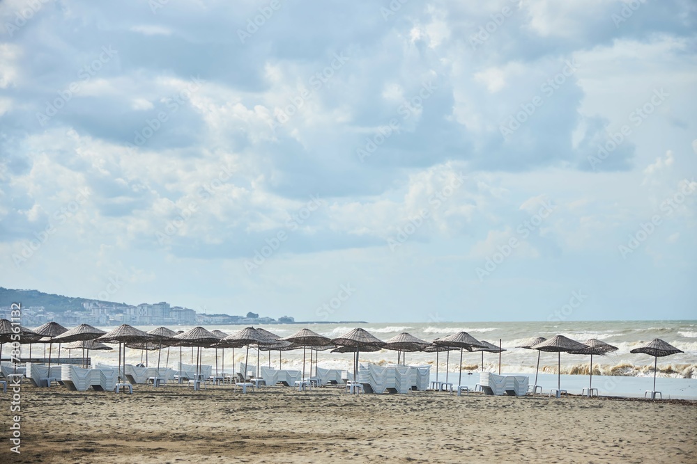 Urban sandy beach by the sea or ocean. Thatched beach umbrellas and sun beds Urban sandy beach by the sea or ocean. Thatched beach umbrellas and sun beds
