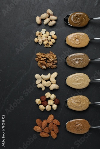 Tasty nut butters in spoons and raw nuts on dark gray textured table  flat lay