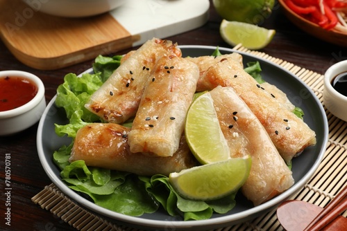 Tasty fried spring rolls, lettuce and sauce on wooden table, closeup