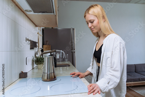 Young woman in a white shirt on the stove making coffee in the kitchen.