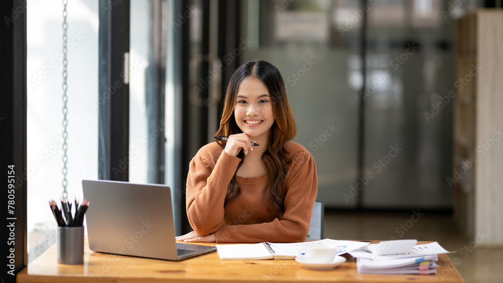 A focused young woman working intently at desk with a laptop and notebook in a bright, modern office setting. A focused young woman working intently at desk with a laptop and notebook in a bright, modern office setting.