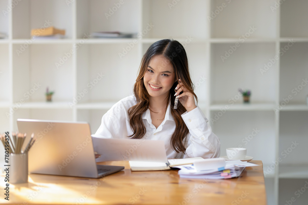 Businesswoman using her smartphone and laptop at office desk with documents and a coffee cup. Businesswoman using her smartphone and laptop at office desk with documents and a coffee cup.