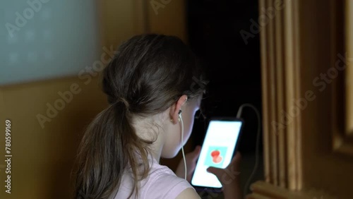 Little girl with a tail plays on a smartphone with wired headphones photo