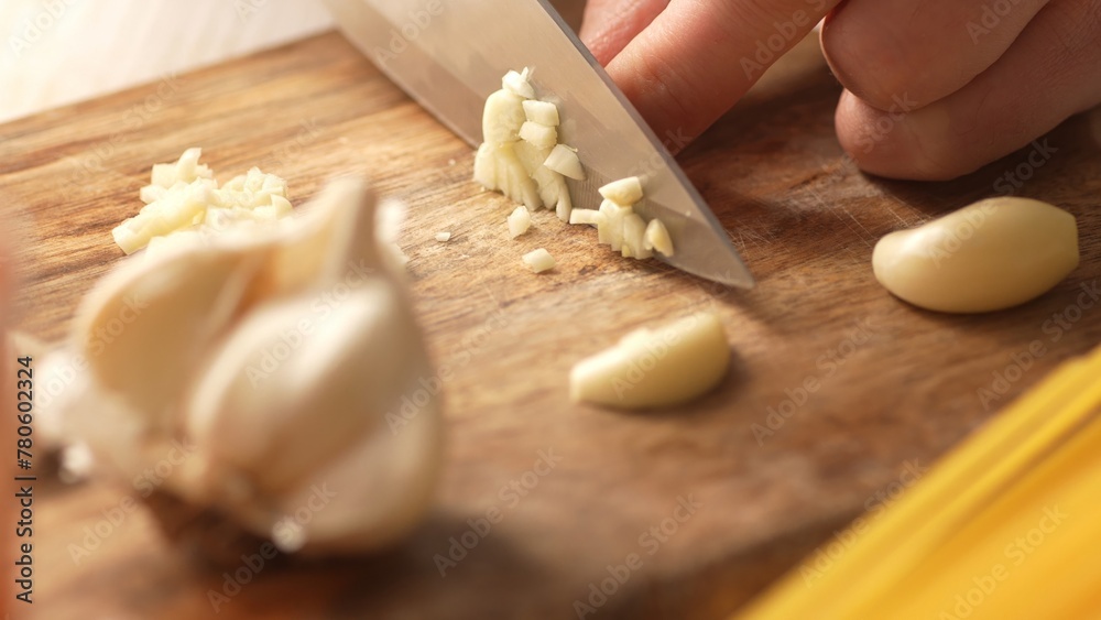 Chopping garlic on a cutting board with pasta. Fried Assassin's Spaghetti Cooking Step. Close-up, shallow dof.