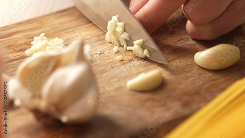 Chopping garlic on a cutting board with pasta. Fried Assassin's Spaghetti Cooking Step. Close-up, shallow dof.