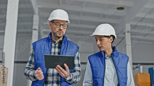 Camera view of two Caucasian workers actively talking with each other while walking on large storage or industrial factory. Handsome man telling something important while young woman disagreeing.