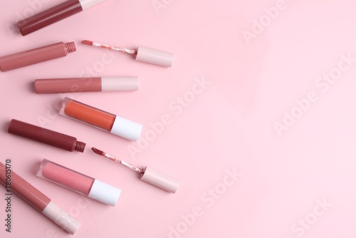 Different lip glosses and applicators on pink background, flat lay. Space for text