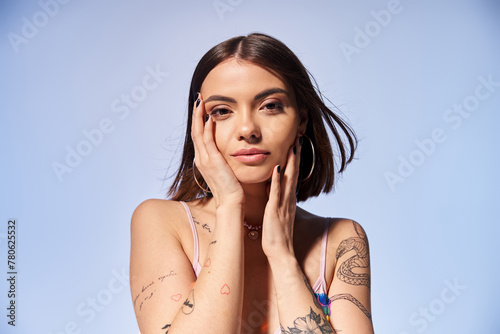A young woman with brunette hair proudly displays a tattoo on her arm while striking a pose in a studio setting. photo