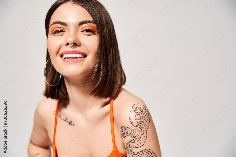 A stylish young woman with brunette hair displaying a beautiful tattoo on her arm in a studio setting. - obrazy, fototapety, plakaty 
