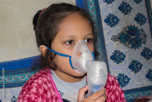 A little girl or child holding a mask nebulizer inhaling medication into lungs at home. Flu, cold Asthma inhaler or nebulizer steam concept