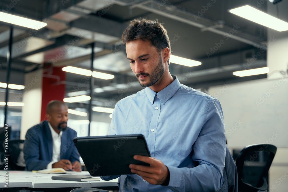 Two multiracial men in businesswear using digital tablet during meeting in office