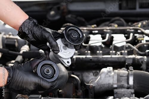 Replacing auto parts in a car. Repairman black gloves holds bypass and parasitic rollers against background of engine compartment and engine. Concept of car maintenance and replacement of spare parts