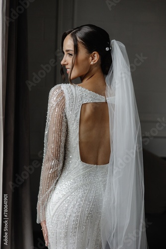 Elegant bride in a white dress with lace and pearls, long veil, and hair pulled back photo