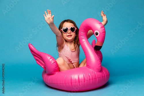 Happy child girl in pink swimsuit with swimming ring flamingo on a colored blue background. Travel, summer beach concept.