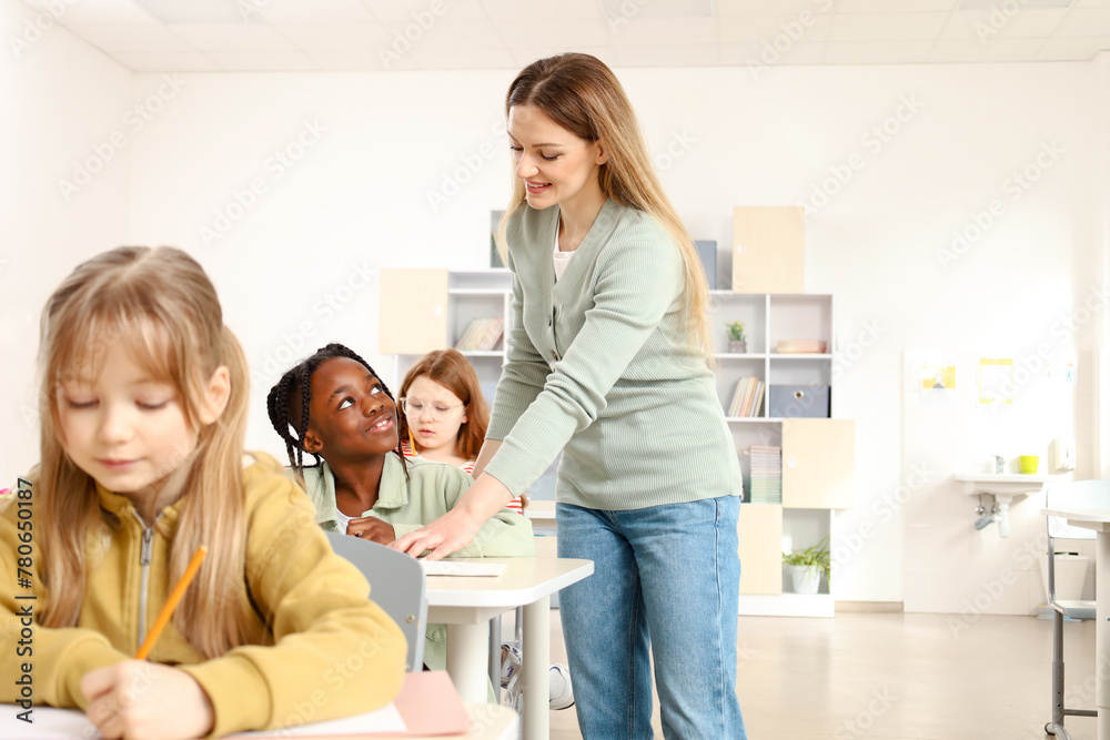 Teacher standing near African American boy while helping her with test in the classroom Teacher standing near African American boy while helping her with test in the classroom