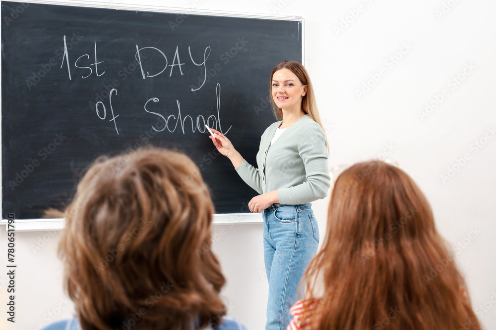 Smiling teacher pointing with hands near chalkboard with first day of school lettering Smiling teacher pointing with hands near chalkboard with first day of school lettering