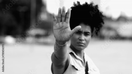 Young woman saying STOP with hand gesture. Person of African Descent showing hand rejecting offer with stern serious expression in black and white photo