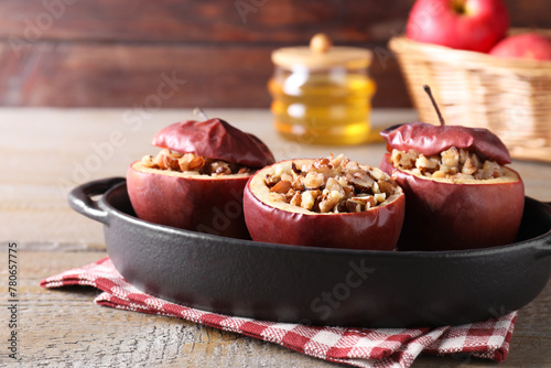 Tasty baked apples with nuts in baking dish on wooden table, closeup