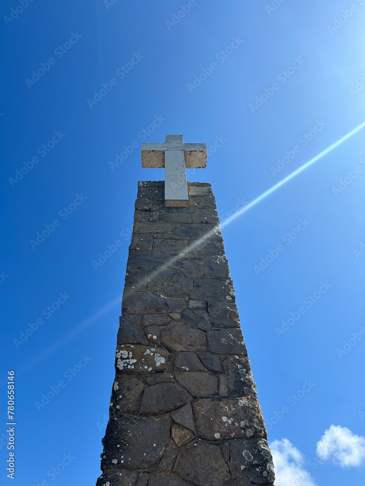 Cross monument at Cabo da Rocca in Portugal against a blue sky with sun flaring across. Cross monument at Cabo da Rocca in Portugal against a blue sky with sun flaring across.