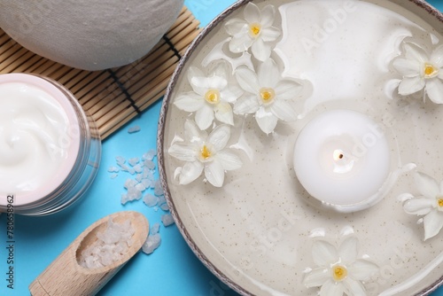 Beautiful composition with spa products  burning candle and flowers on light blue background  flat lay