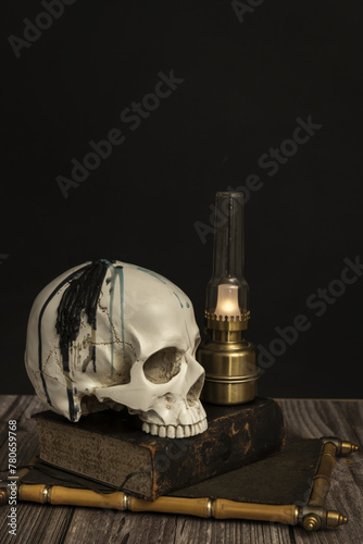 a still life with a white skull with upper teeth on an old book next to a small Argand lamp on a wooden table photo